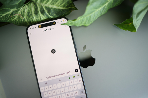 Smartphone displaying the ChatGPT app on top of a closed laptop, with plant leaves partially framing the device, representing mobile AI or digital productivity.