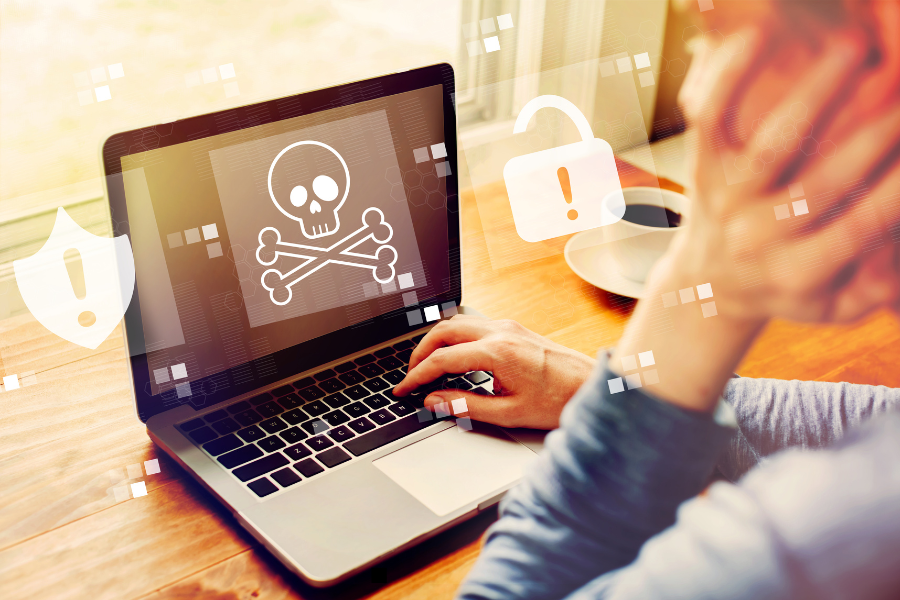 Person using a laptop showing a malware symbol on the screen with lock and warning icons overlaid, illustrating cybersecurity risks and online scams.