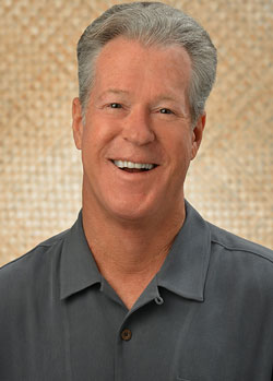 A professional headshot of a person wearing a dark gray collared shirt, photographed against a textured beige background.