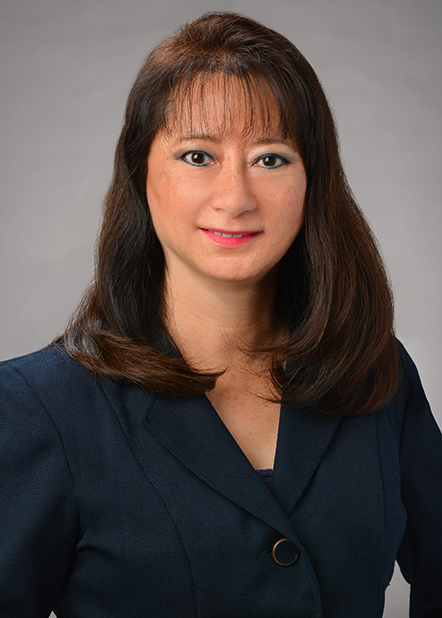 A professional headshot of a person wearing a navy business suit, photographed against a gray studio background.