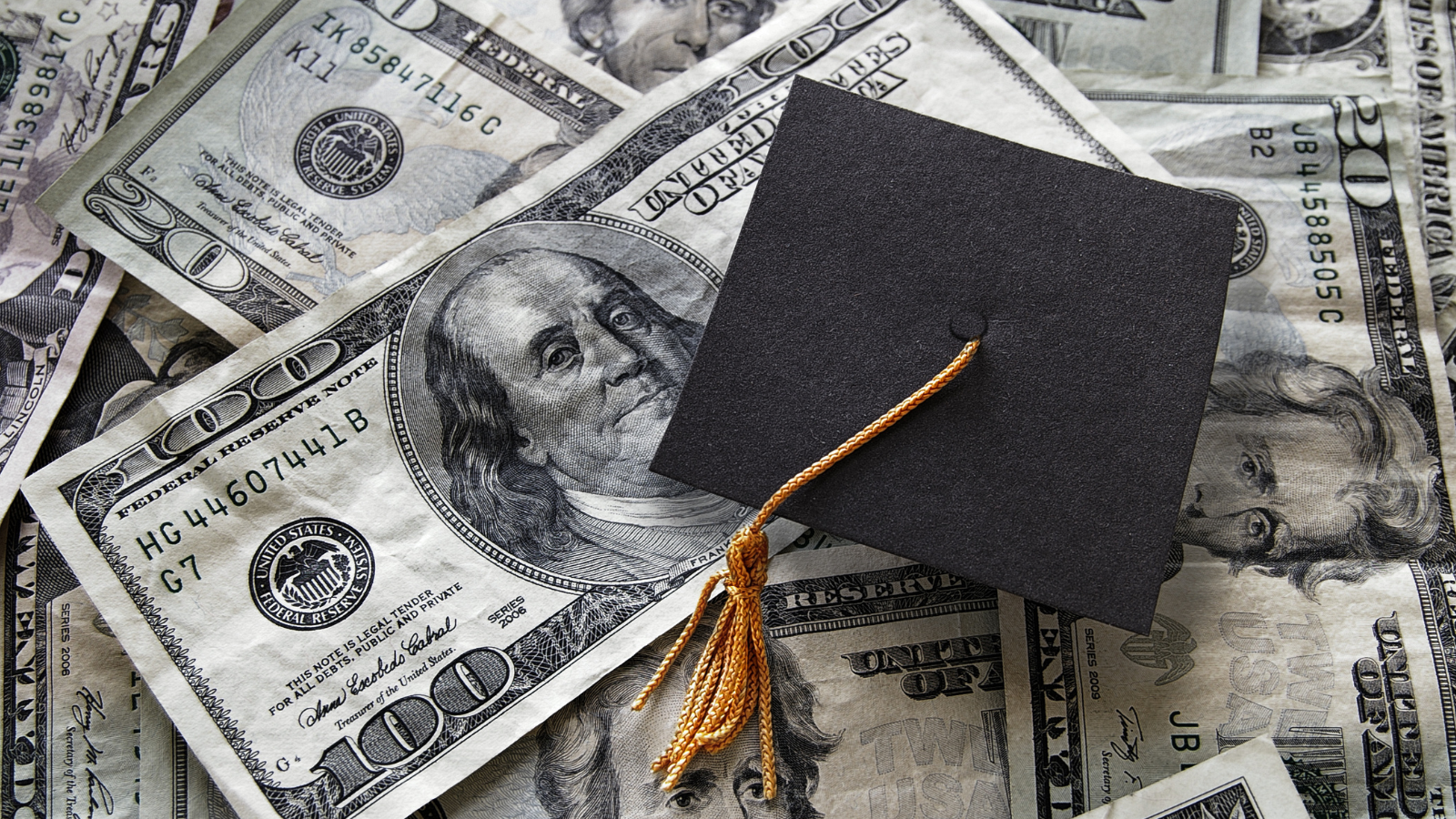 Graduation cap resting on U.S. dollar bills, symbolizing the cost of higher education, student loans, and college savings.