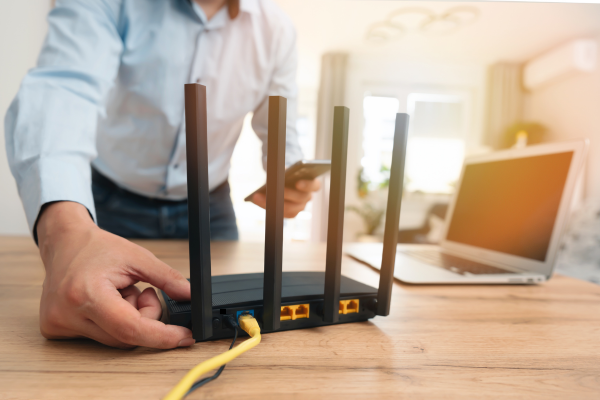 Person setting up a wireless router by connecting an Ethernet cable, with a smartphone and laptop nearby, representing home internet or network security.