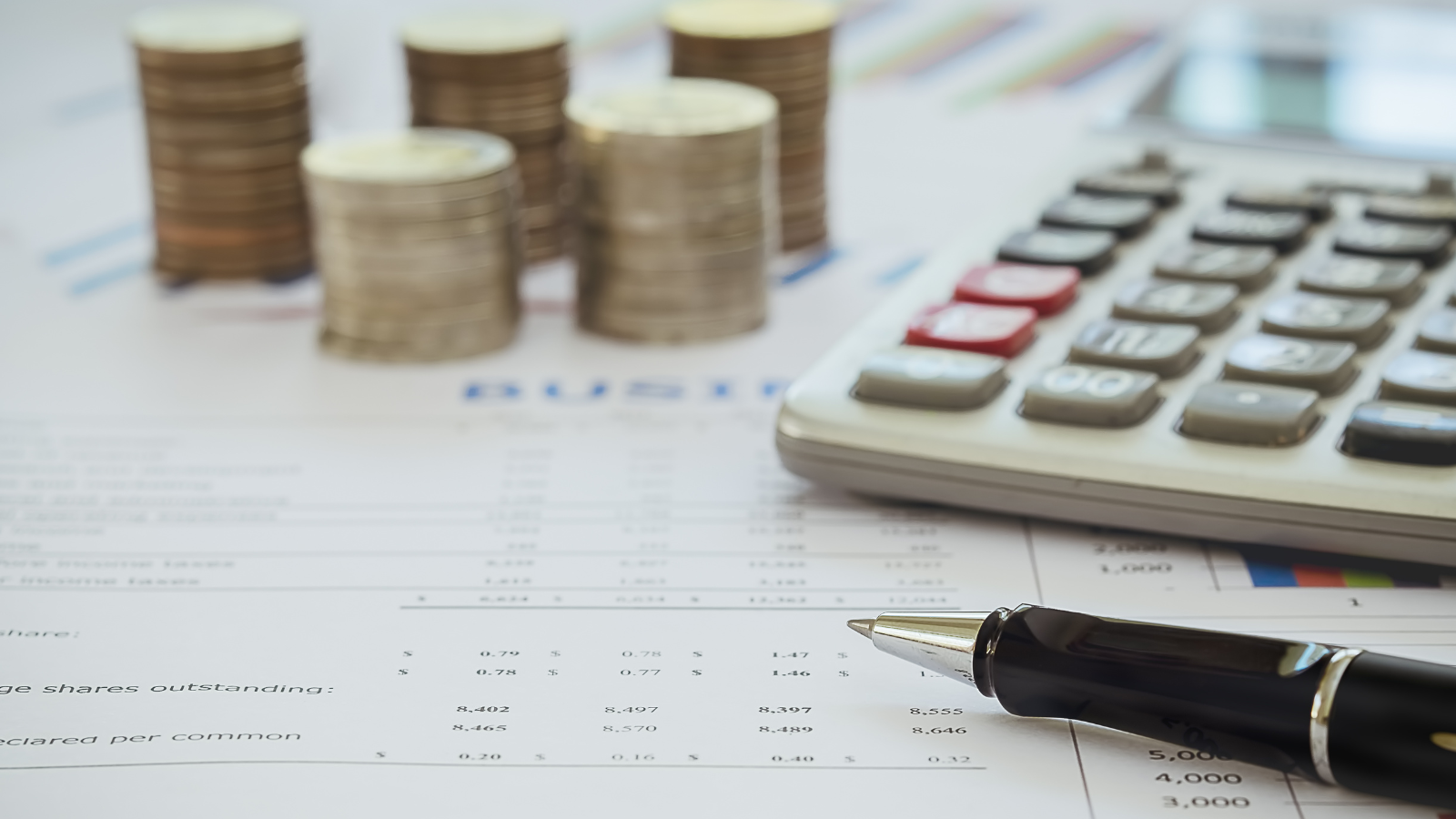Calculator, stacks of coins, and financial documents on a desk.