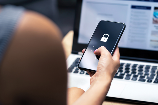 Close-up of a person unlocking a smartphone with a passcode while using a laptop, representing account security and device protection.