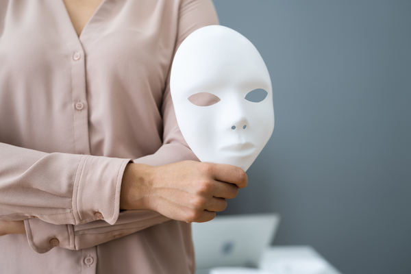 Close-up of a person holding a blank white mask in an office setting, illustrating identity theft, impersonation, or fraudulent activity.