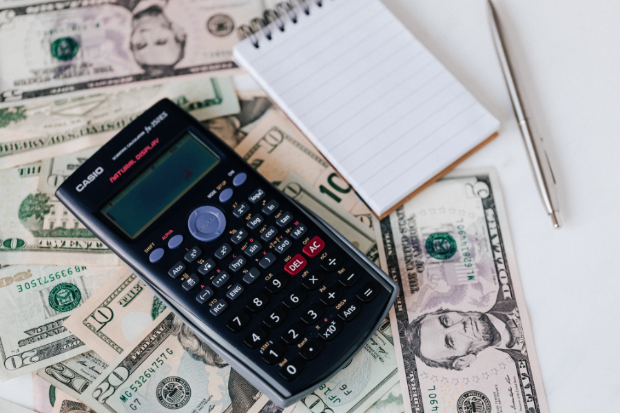 Calculator resting on U.S. currency beside a notepad and pen, illustrating budgeting, expense tracking, and financial planning.