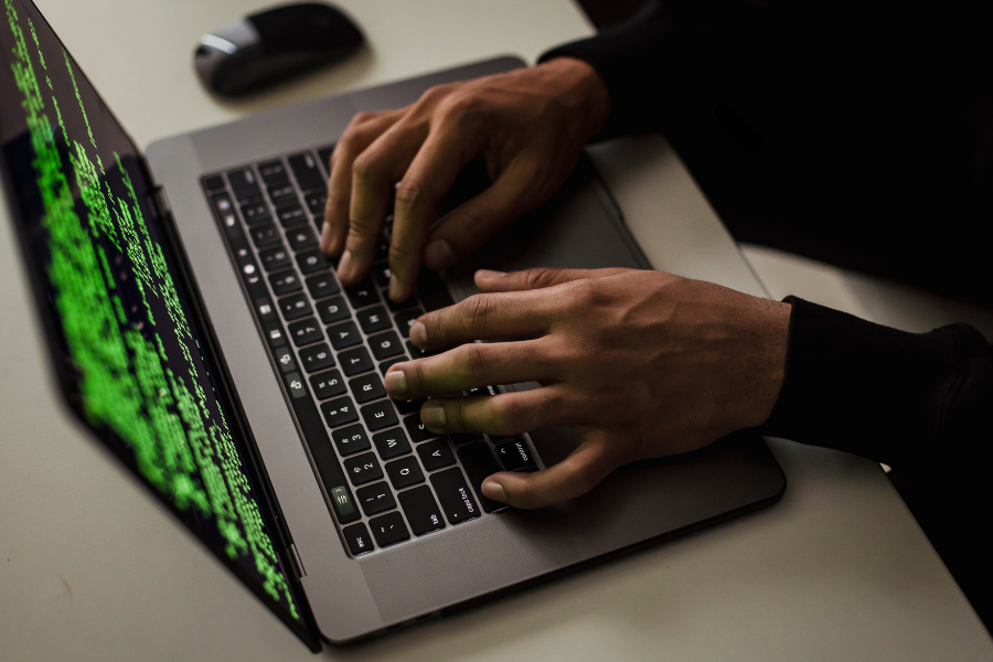 Close-up of a person typing on a laptop with green code displayed on the screen, illustrating cybersecurity threats or cybercrime.