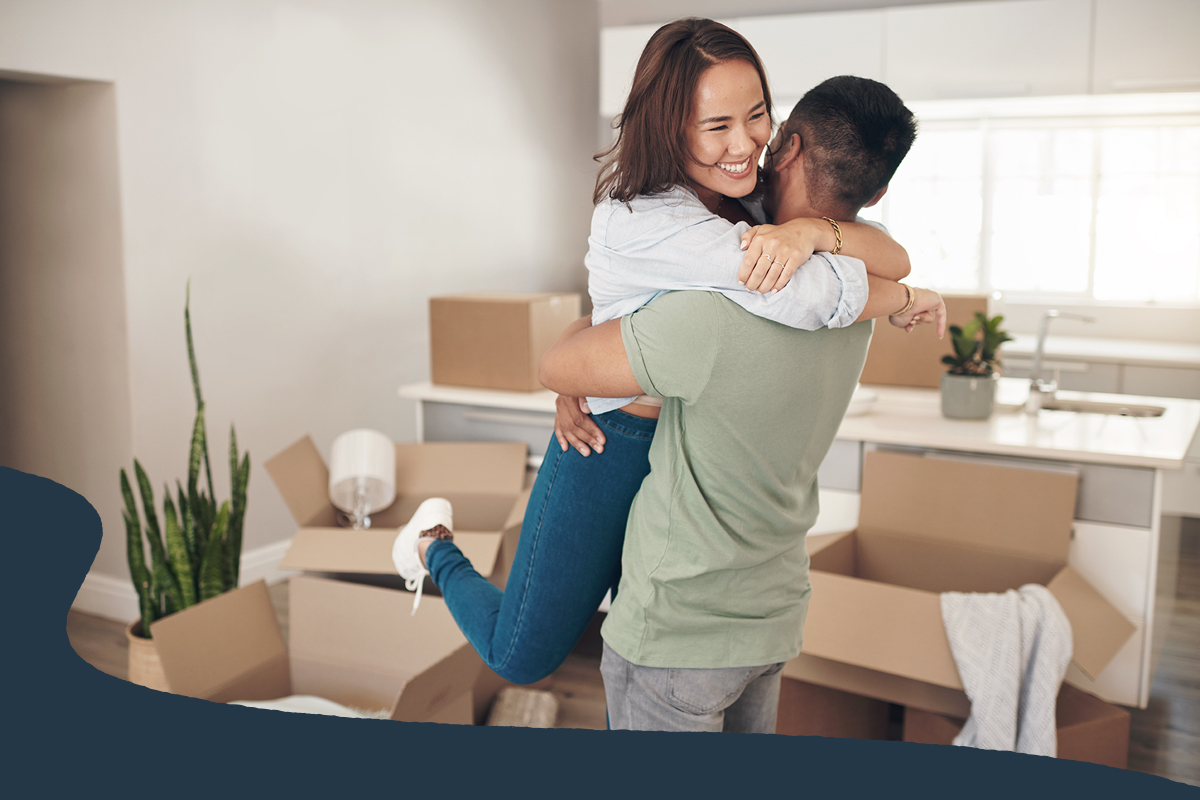 Couple embracing in a new home surrounded by moving boxes.