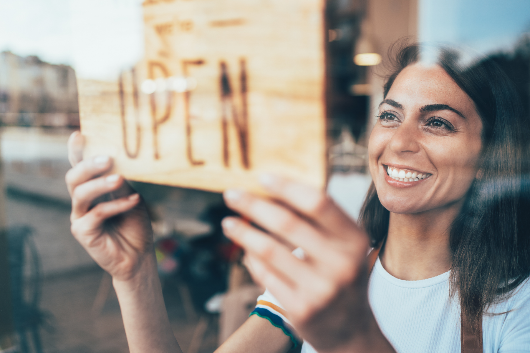 Smiling small business owner hanging an "Open" sign in a shop window to welcome customers.