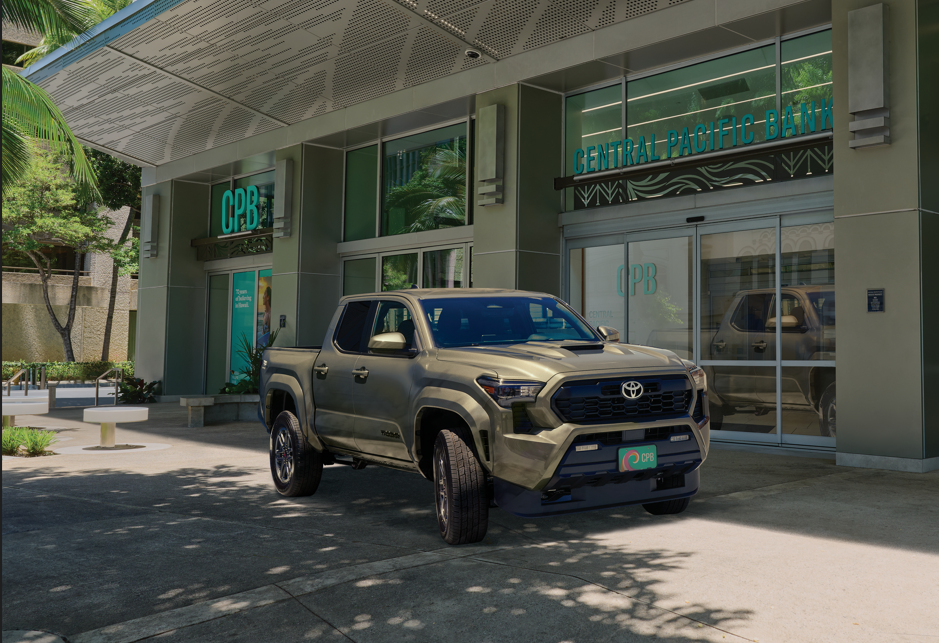 A Toyota Tacoma pickup truck is parked outside a Central Pacific Bank branch, with CPB signage prominently displayed above the entrance. The modern bank building features large glass windows, tropical landscaping, and contemporary architectural details.