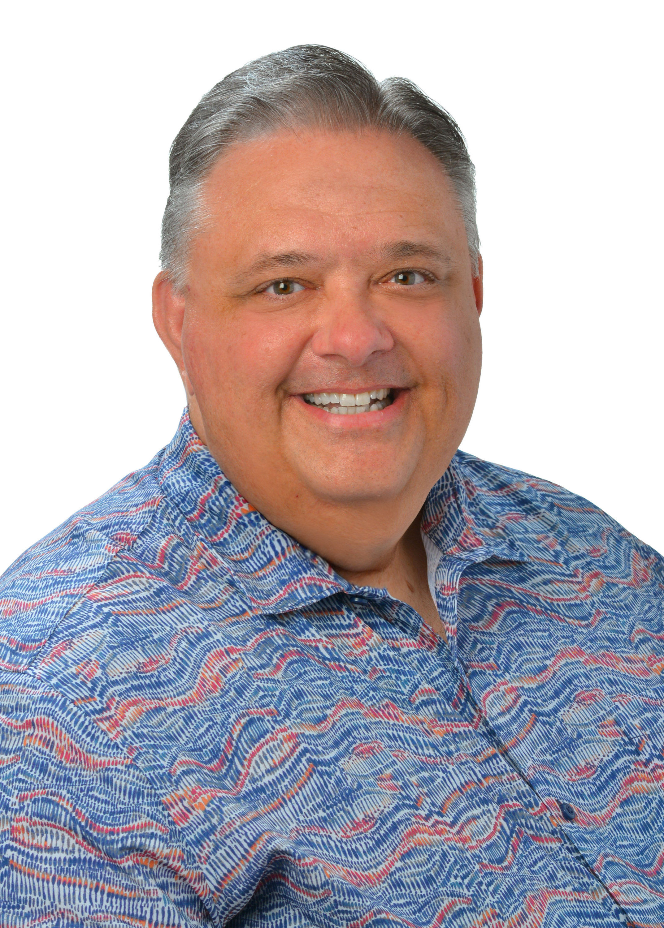 A professional headshot of a person with short gray hair wearing a blue patterned aloha shirt, photographed against a light gray background.