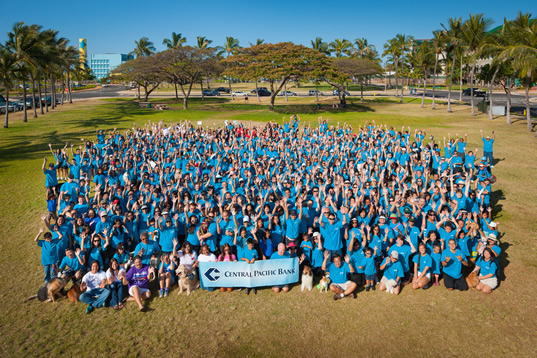 A group of CPB workers in matching shirts huddled together to take a photo at a park.