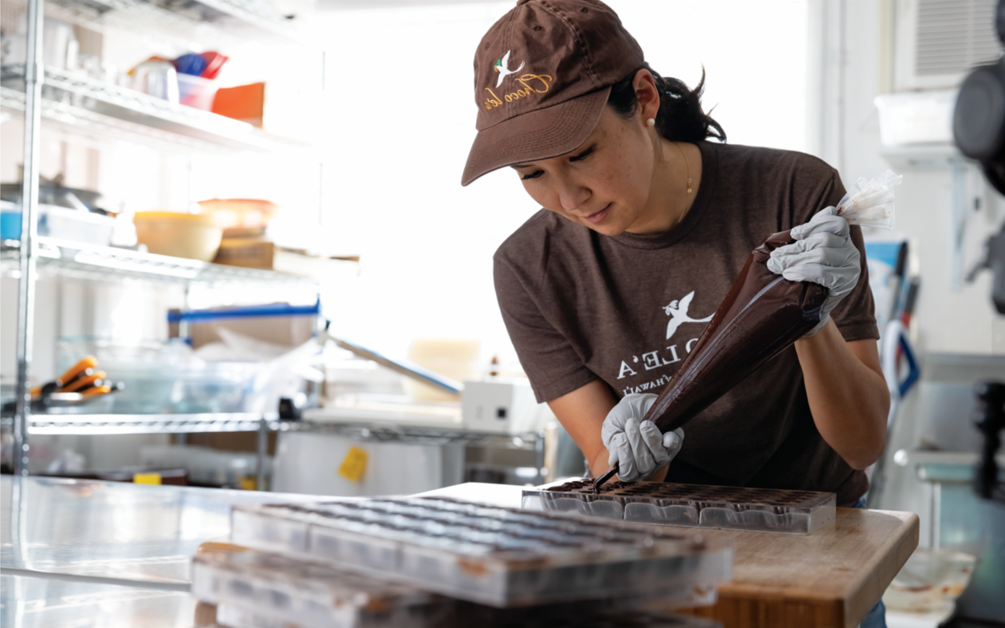 Small business owner carefully filling chocolate molds by hand in a commercial kitchen.