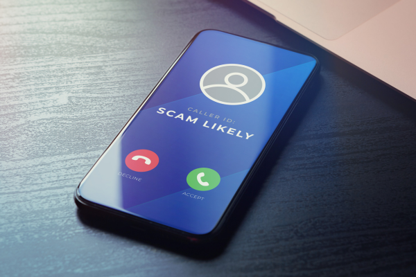 Close-up of a smartphone showing an incoming call labeled "Scam Likely," with accept and decline buttons, representing phone scam awareness.