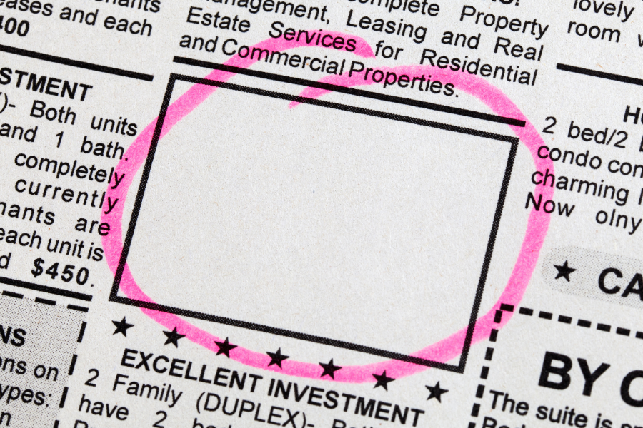 Close-up of a newspaper's real estate classified section with a blank property listing highlighted by a pink circle.