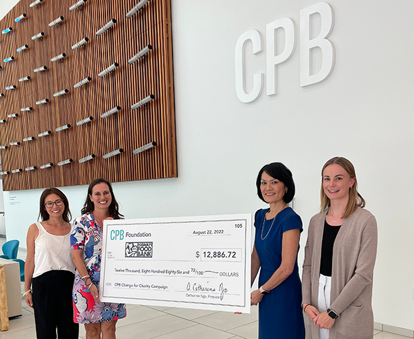 Four people stand in the Central Pacific Bank lobby presenting a CPB Foundation donation check for $12,886.72 to the Hawaii Foodbank. The group poses beneath the large CPB logo and a decorative wood wall installation during the check presentation ceremony.
