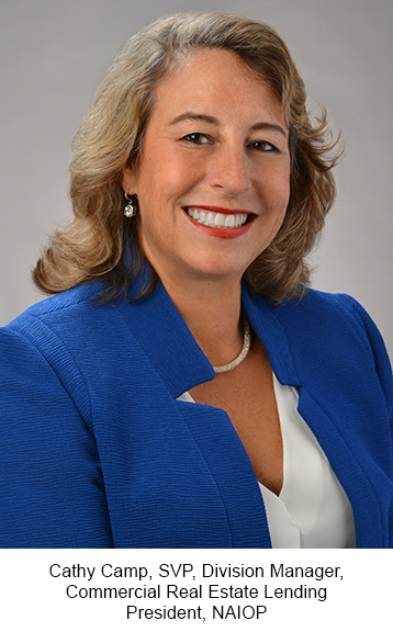 A professional headshot of a person wearing a blue blazer over a white blouse, photographed against a gray studio background. Text below the photo identifies the individual as Cathy Camp, SVP, Division Manager, Commercial Real Estate Lending, and President of NAIOP.
