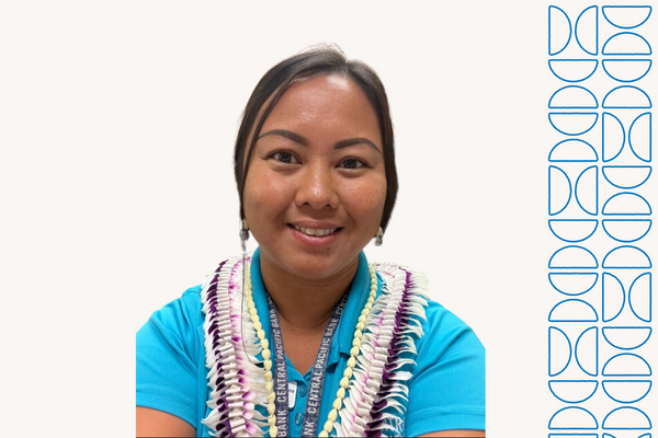 A professional portrait of a person wearing a teal polo shirt and multiple flower leis, photographed against a light gray background. A blue geometric design element appears along the right side of the image.