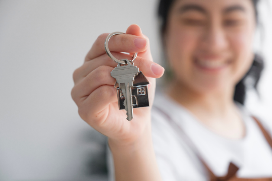 Smiling new homeowner holding a key ring with a house-shaped keychain, representing the purchase of a new home.