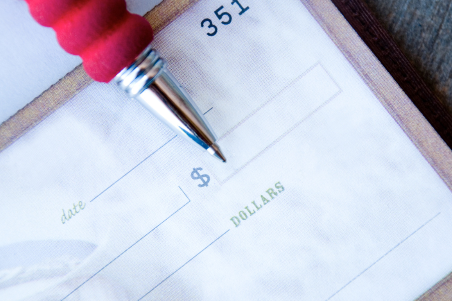 Close-up of a pen positioned over the amount section of a blank check, representing check writing or financial transactions.