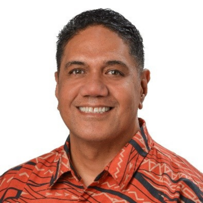 A professional headshot of a person wearing a red aloha shirt with a black geometric pattern, photographed against a light gray background.