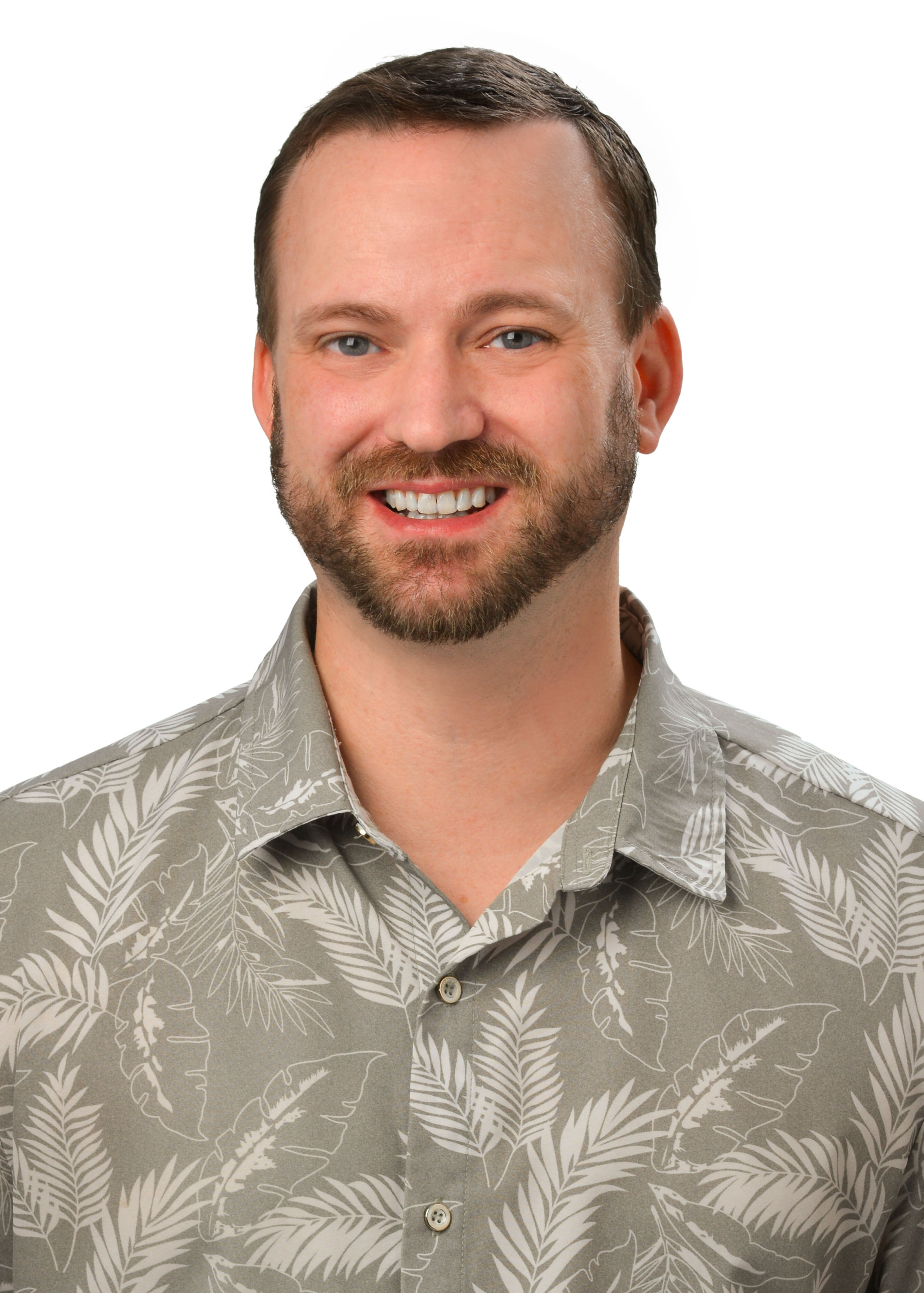 A professional headshot of a person with a beard wearing a light gray aloha shirt with a tropical leaf pattern, photographed against a light gray background.