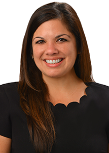 A professional headshot of a person wearing a black blouse with a scalloped neckline, photographed against a light gray background.