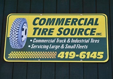 Yellow and green "Commercial Tire Source Inc." sign mounted on a building exterior advertising commercial truck and industrial tires, fleet services, and a contact phone number.