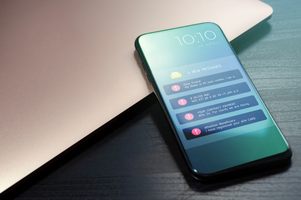 Close-up of a smartphone showing multiple account security and fraud alert text messages next to a laptop, representing mobile banking security and scam awareness.