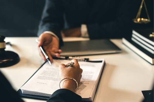 Person signing a document across a desk while another person points to the paperwork during a meeting.